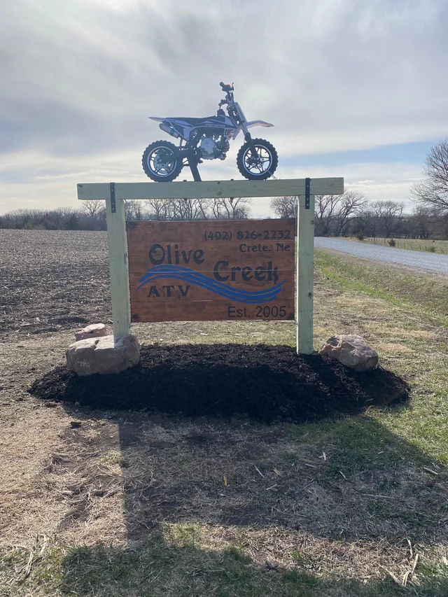 A dirt bike mounted above the wooden Olive Creek ATV sign at the driveway entrance
